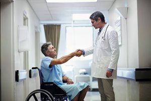 Shot of a doctor shaking hands with a patient in a wheelchair in a hospital corridor